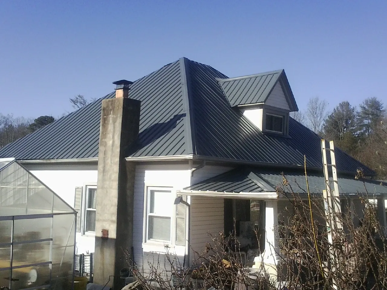 Dark blue standing seam metal roof on a white farmhouse with dormer — Slate & Tile Roof Repair by Roofing Brothers in Jonesboro