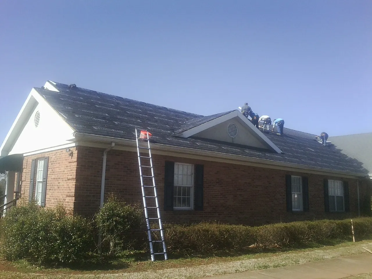 Crew tearing shingles off a brick ranch roof with a ladder set — Metal Roof Repair work by our crew in Jonesboro