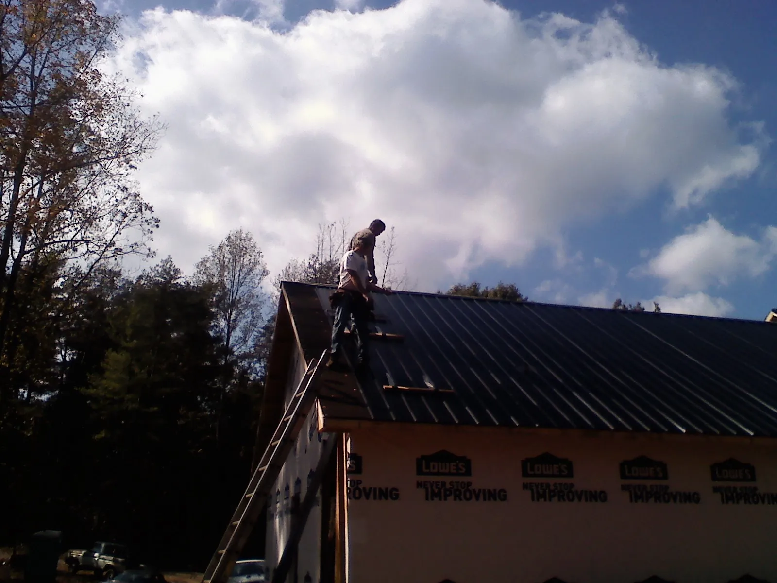 Roofer fastening dark metal panels high against a cloudy sky, from a Roof Inspection job in Jonesboro